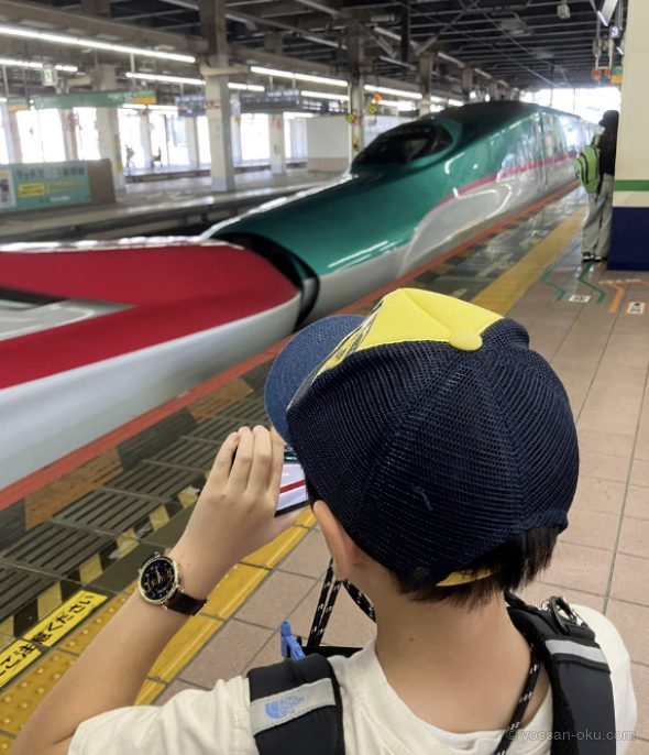 駅のホームで連結した新幹線を撮影する小学生の息子